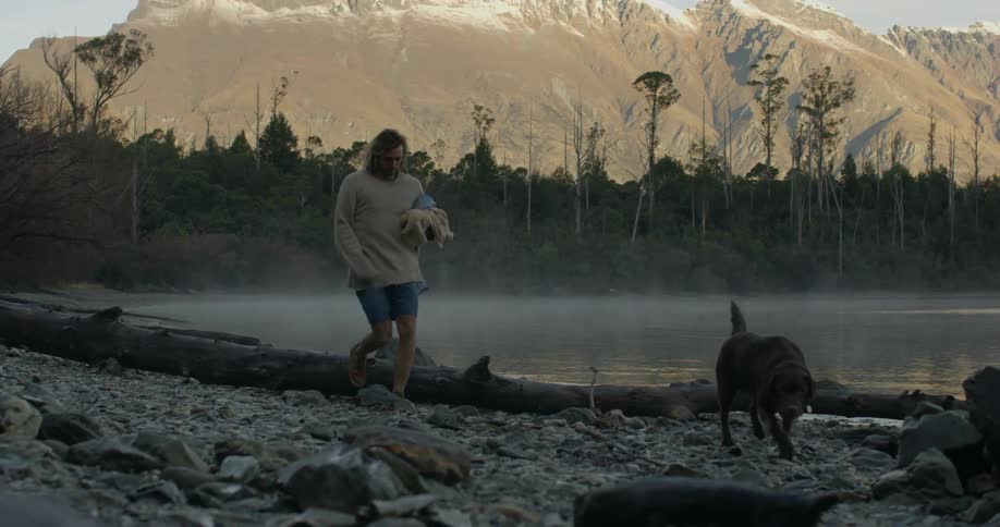 A man walks along with his dog by the lake