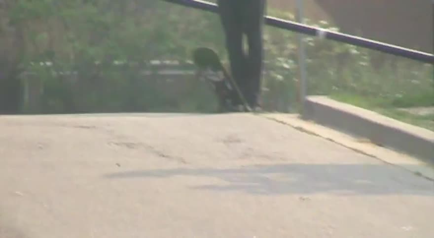 A man with a skateboard stands by a parking gate as a car drives by in this grainy, shaky footage