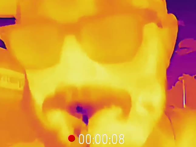 A close-up thermal camera captures a man in a hat and sunglasses pouring cold water on his face to cool off
