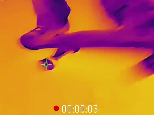 Thermal vision footage follows a skateboarder's feet in slow motion as they land a kickflip trick on a street