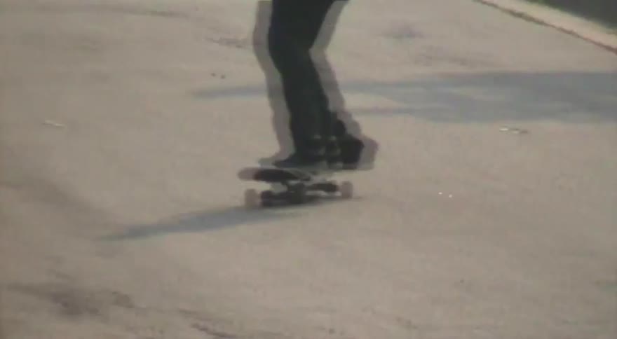 A vintage-style close-up of a person's feet as they skateboard on a paved surface
