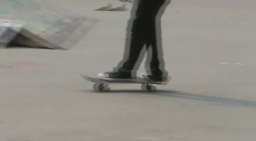 Close-up, shaky vintage footage follows a person's feet as they skateboard around a concrete skatepark