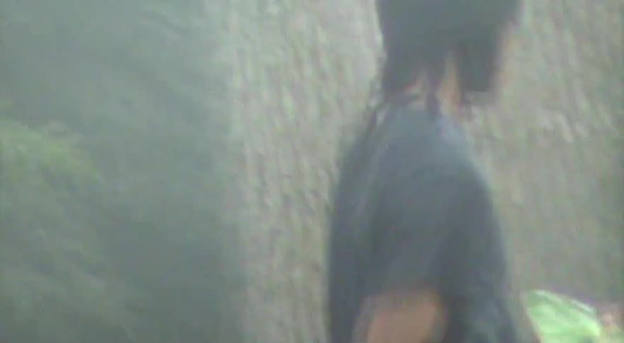 A young man with dreadlocks carries his skateboard as he walks through a foggy, dreamlike park