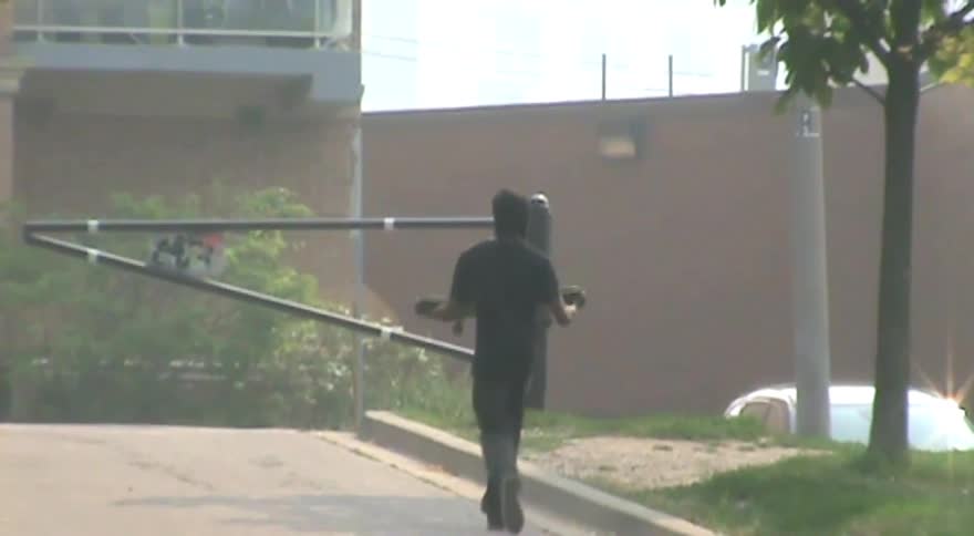 Rear view of a person in dark clothing walking away down a paved road while carrying a skateboard