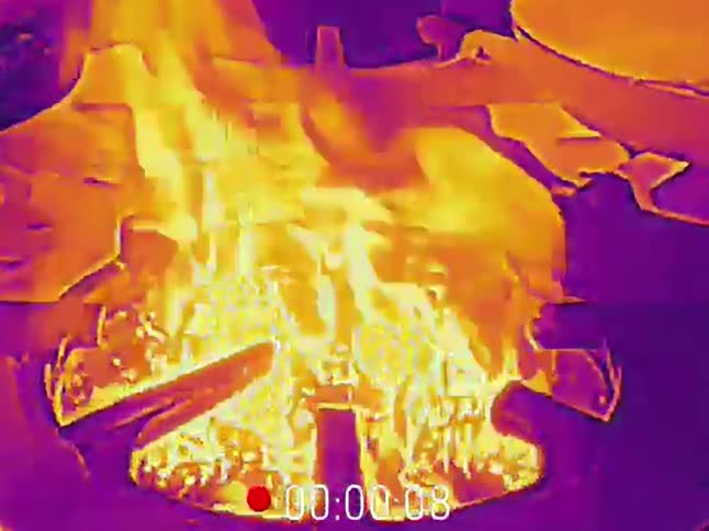 A close-up thermal imaging view shows a fire being lit and burning brightly in a small fire pit