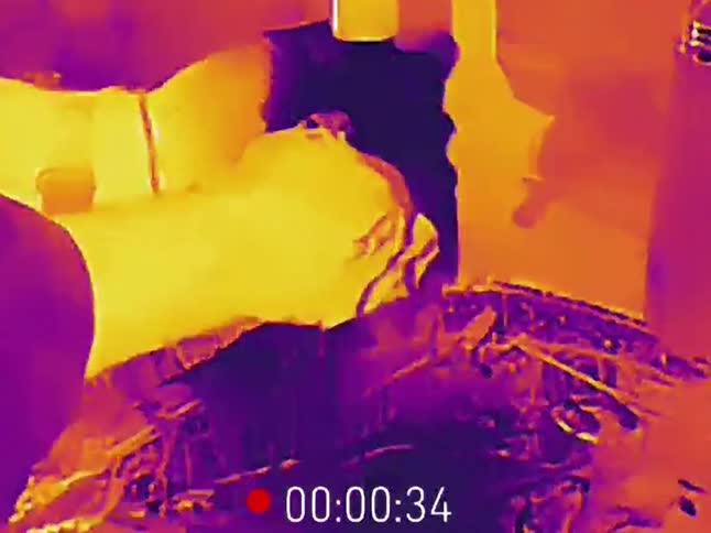 A close-up thermal imaging view of a mechanic's hands working on a complex engine in a workshop