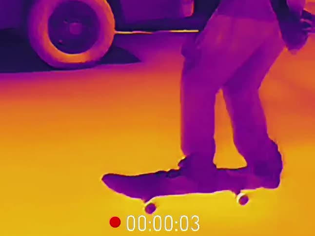 Thermal camera footage shows a skateboarder failing a trick while riding on a suburban street at night
