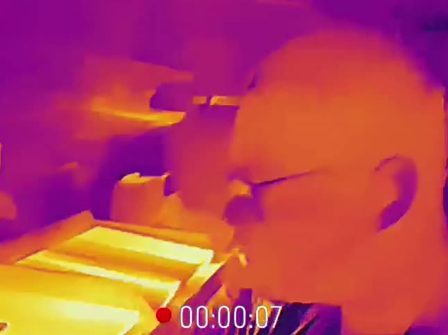 A person cooks a meal on the stove, viewed through a found-footage style thermal camera