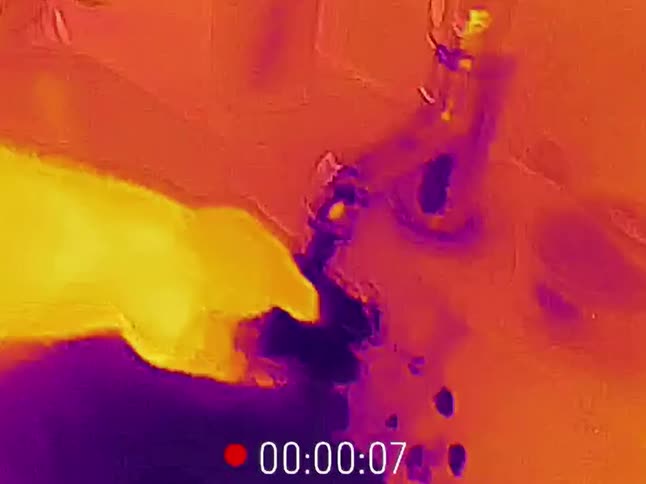 An artistic thermal camera view shows a hand turning on the hot water in a bathroom sink