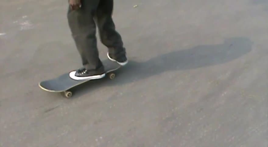 A skateboarder attempts a kickflip in slow motion but fails to land the trick on the asphalt