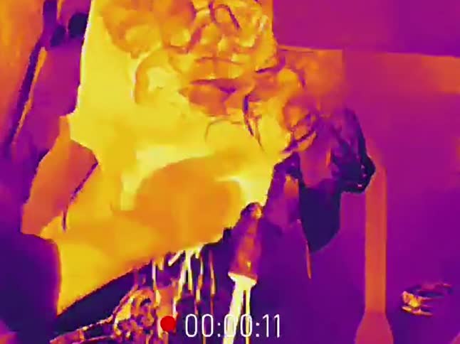 Experimental thermal camera footage captures a close-up of a man eating while dishes are washed in a sink