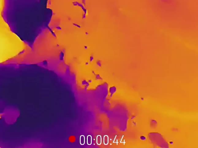A thermal imaging camera captures the heat of hot water running from a tap as a person washes a brush in the sink