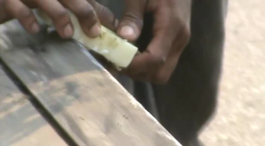 A detailed close-up shot of a person's hands rubbing a bar of wax along the base of a snowboard to prepare it for riding