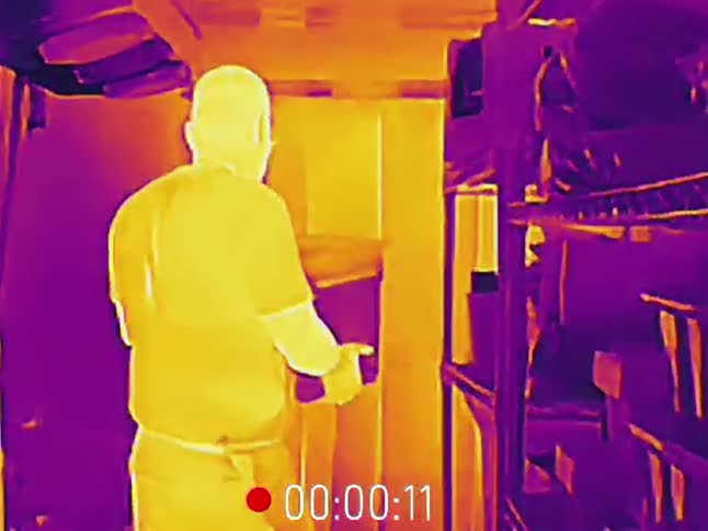 Thermal imaging footage shows a worker passing through plastic curtains into a cold storage area to retrieve a box