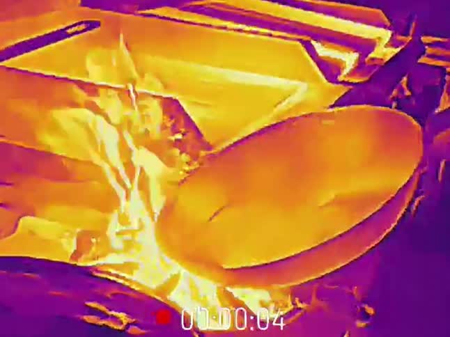 A dramatic thermal imaging view shows a chef flambéing food in a hot pan in a professional kitchen