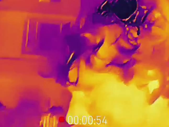 A person sings into a microphone while holding a child on their shoulders, as seen through a thermal imaging camera