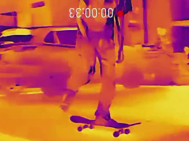A person skateboards at night and performs a trick, captured through the unique lens of a thermal imaging camera