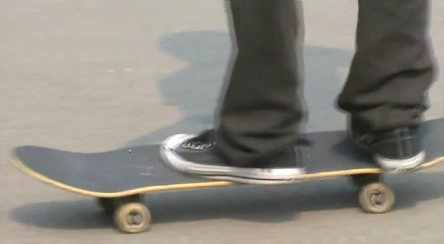 Slow motion close-up of a person's feet successfully landing a kickflip on a skateboard at a skate park
