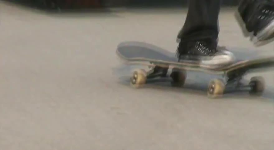 A shaky close-up follows a skateboarder's feet as they cruise through a skate park and ride over a small ramp