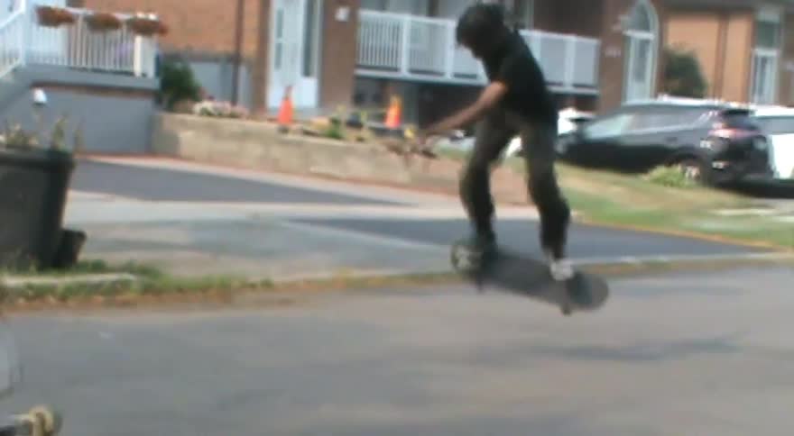 Slow motion footage shows a skateboarder landing a kickflip on a paved street