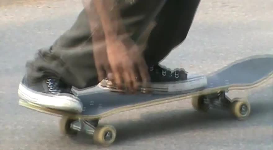 A close-up of a skateboarder's feet in sneakers attempting a flip trick and failing on an asphalt street