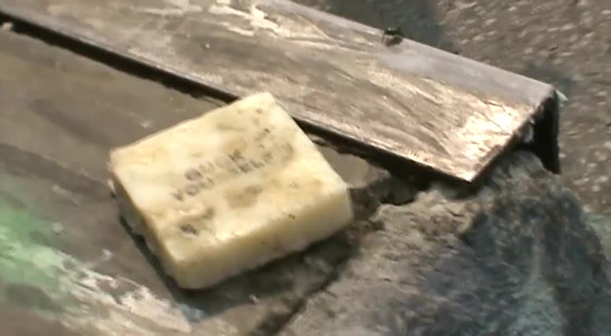 Close-up of a dirty block of skateboard wax with the text 'GUCK YOURSELF' on a concrete skate ledge