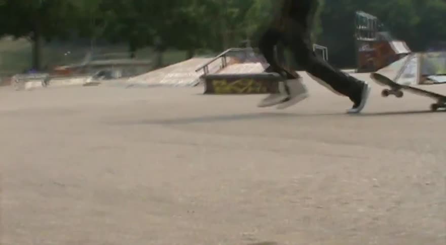 A young man with dreadlocks lands a kickflip at a hazy skatepark and runs off as the camera focuses on his board