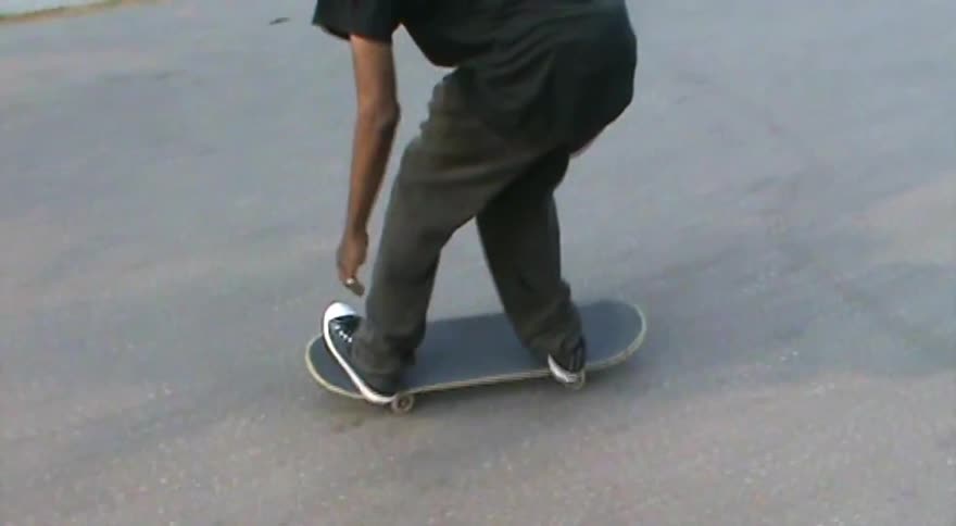 A skateboarder's feet are seen in a slow-motion close-up as they successfully land a kickflip on a paved street