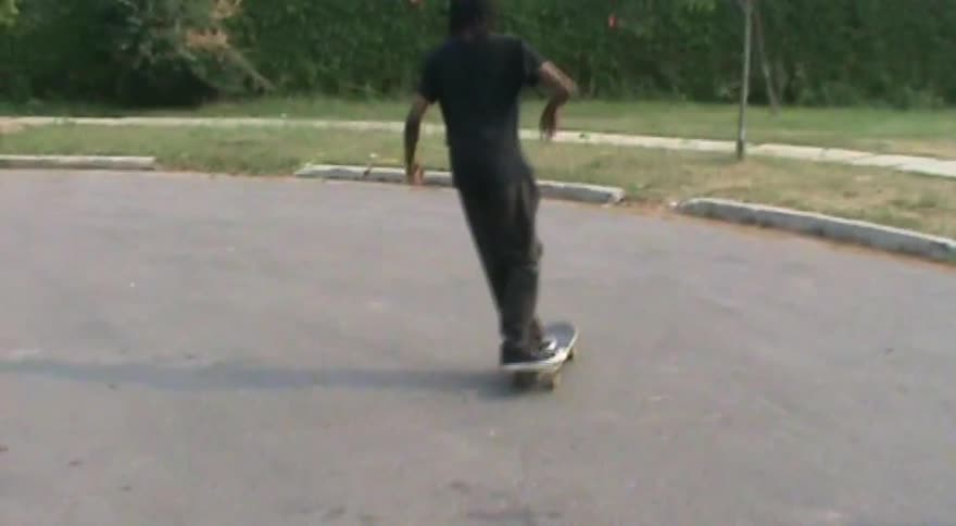A skateboarder performs a kickflip and a pop shove-it in slow motion on an empty suburban street