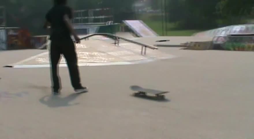 A skateboarder falls while attempting a rail grind at a skatepark, and the camera follows the runaway board