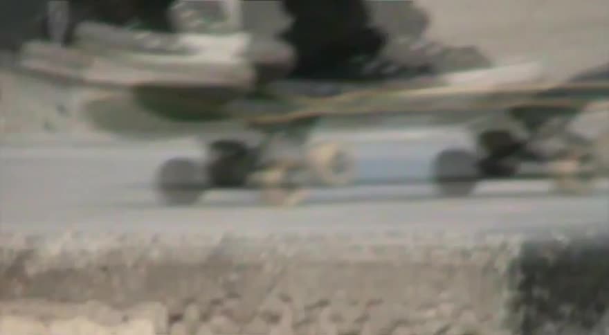Vintage-style close-up footage tracks a skateboarder's feet as they ride and attempt a trick in a skatepark