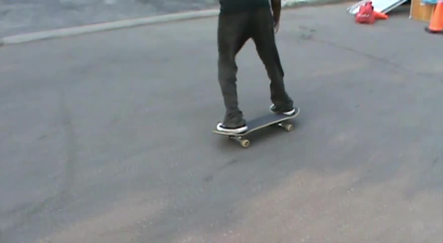 A skateboarder is captured in slow-motion footage successfully executing a kickflip on a paved surface
