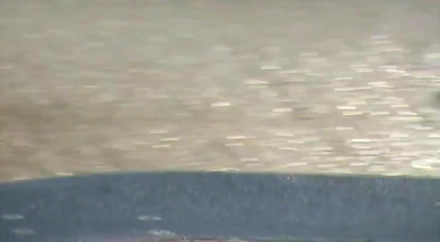 A skateboarder riding down a sidewalk is caught in a sudden, heavy downpour and stops