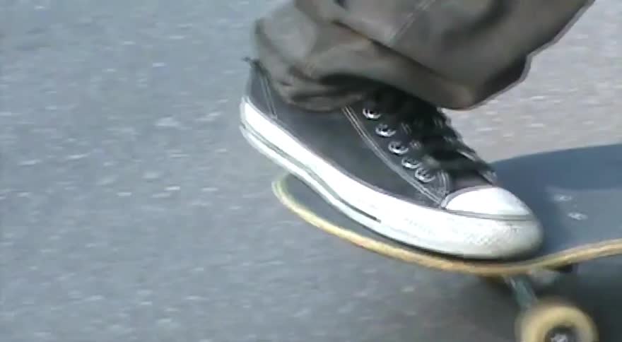 Shaky, vintage-style home video footage captures a person skateboarding on a paved street