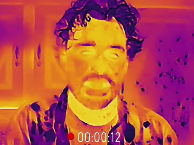 A man sneezes as seen through a thermal camera, showing the spray of droplets
