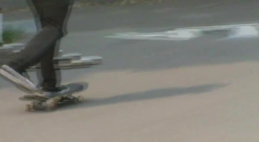A low-angle shot follows a skateboarder's feet as they attempt a kickflip off a ledge in a graffiti-covered skatepark