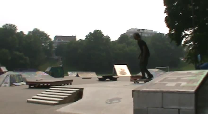 Vintage-style footage of a skateboarder showing off his skills and landing a kickflip at a public skatepark