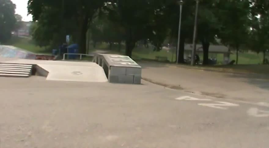 A skateboarder executes a kickflip in slow motion at an outdoor skatepark
