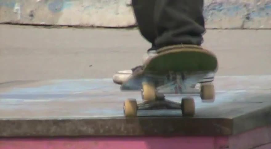 A gritty, vintage-style close-up of a skateboarder's feet performing tricks at a concrete skatepark