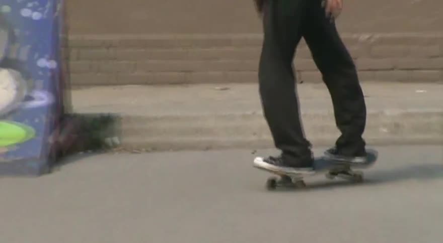 Grainy, retro-style footage captures a young man performing a kickflip trick on his skateboard at an urban skatepark