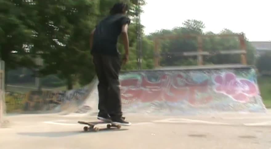 A skateboarder performs a grind on a ledge and rides a half-pipe at an urban skatepark in slow motion