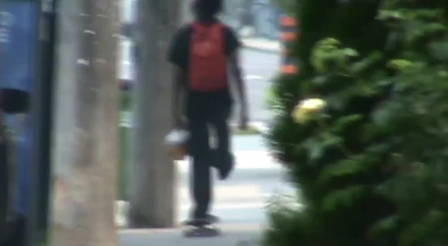 A person with a red backpack skateboards away down a city sidewalk in a dreamy, distorted long shot
