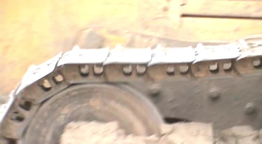 Close-up shot of the muddy continuous tracks of a bulldozer rolling over dirt at a construction site