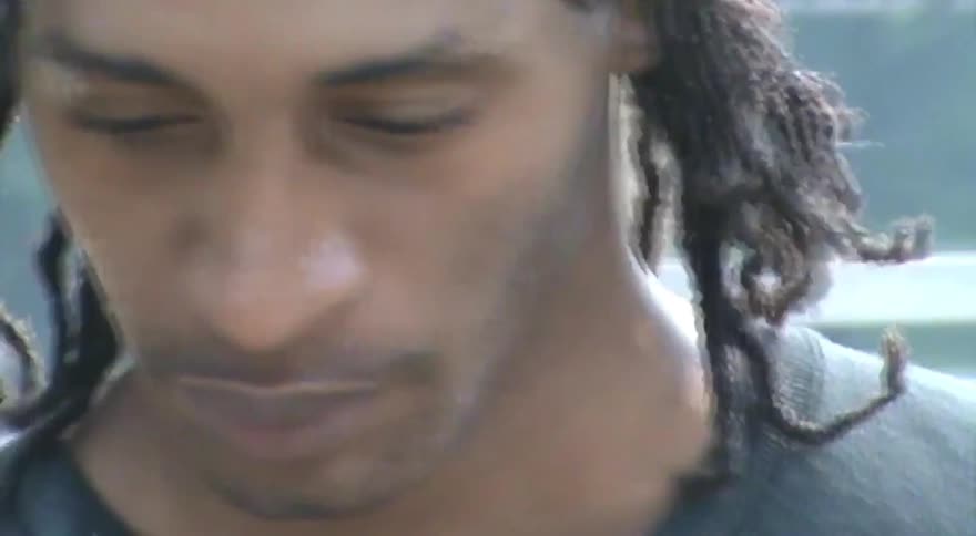 A close-up shot of a young man with dreadlocks wiping his face before placing skateboard wax on a concrete ledge