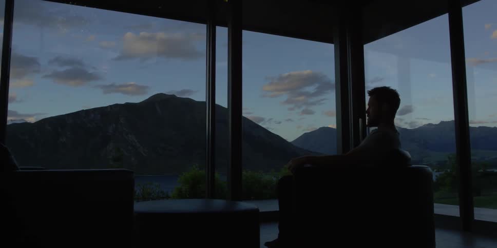 Man looks out a large window at mountains