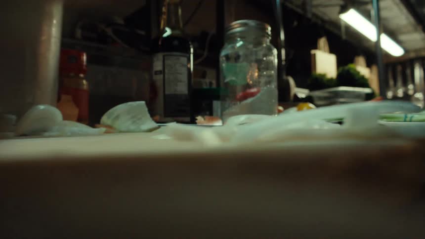 A close-up, low-angle shot shows a chef's hands scooping up a pile of freshly sliced onions from a cutting board in a kitchen
