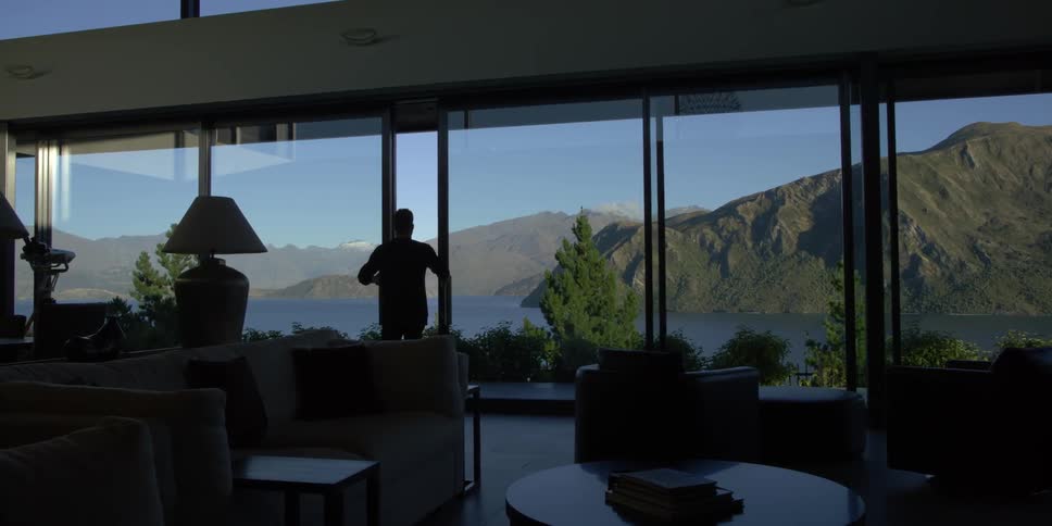A man close a sliding glass door overlooking a mountain lake