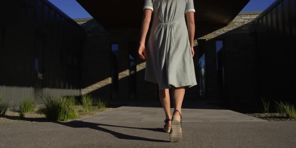 A woman in sandals and a dress walks towards a building
