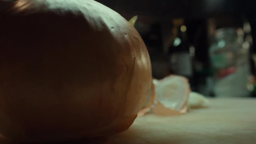 A dramatic, low-angle close-up shot of a chef's hands peeling an onion with a sharp knife on a wooden cutting board