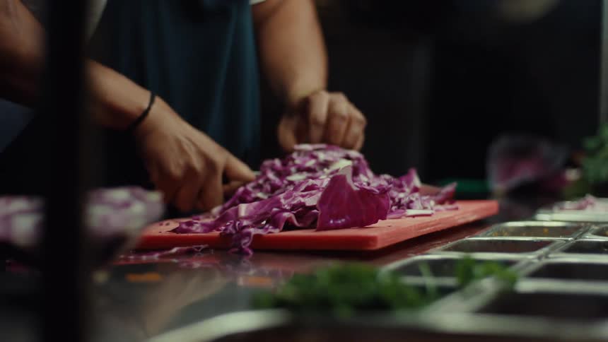 Close up shot of a chef's hands rapidly chopping vibrant red cabbage on a stainless steel prep counter in a commercial kitchen